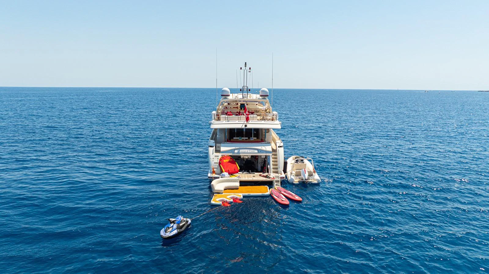 The yacht is anchored in calm blue waters, showcasing its array of water toys and tenders at the stern. aboard CHAMPAGNE AND CAVIAR Yacht for Sale