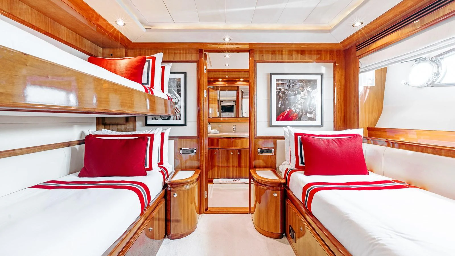 The twin stateroom features two single beds with elegant red and white bedding, complemented by rich wood paneling and modern lighting. aboard CHAMPAGNE AND CAVIAR Yacht for Sale
