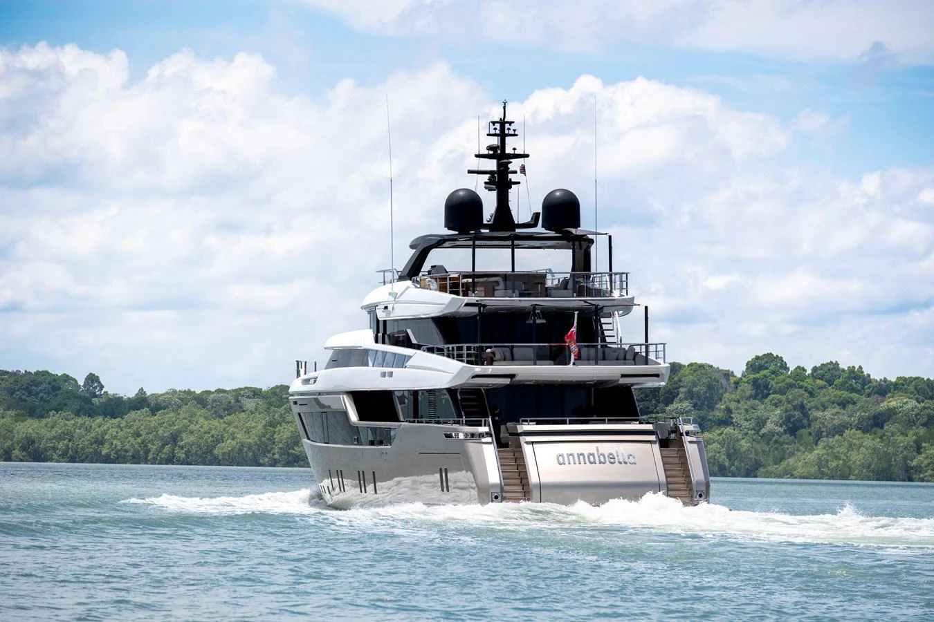 A luxurious yacht cruises through calm waters against a backdrop of lush greenery and a partly cloudy sky. aboard ANNABELLA Yacht for Sale