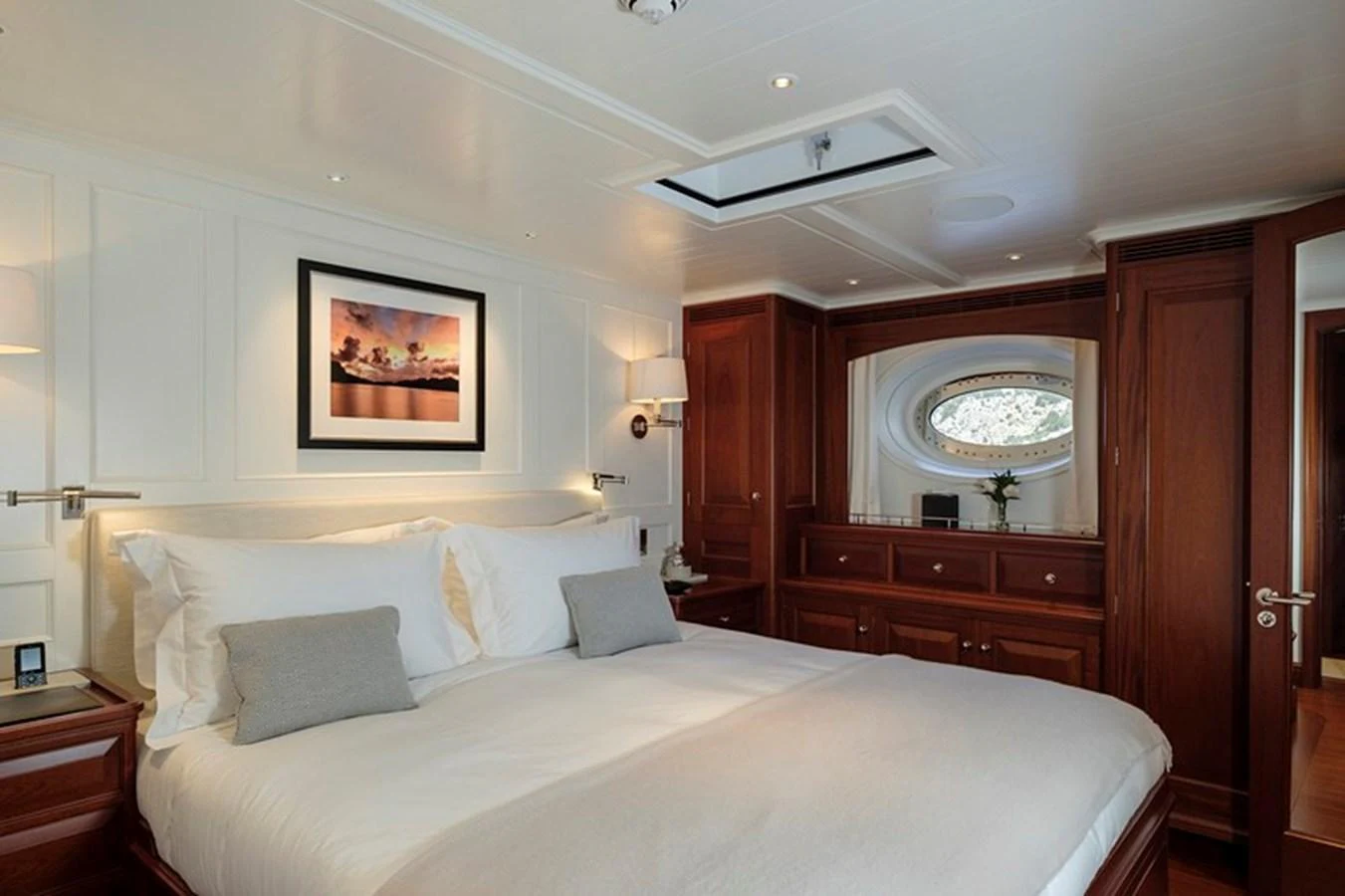 The master stateroom features elegant wood paneling, a large bed, and a scenic porthole view. aboard APSARA Yacht for Sale