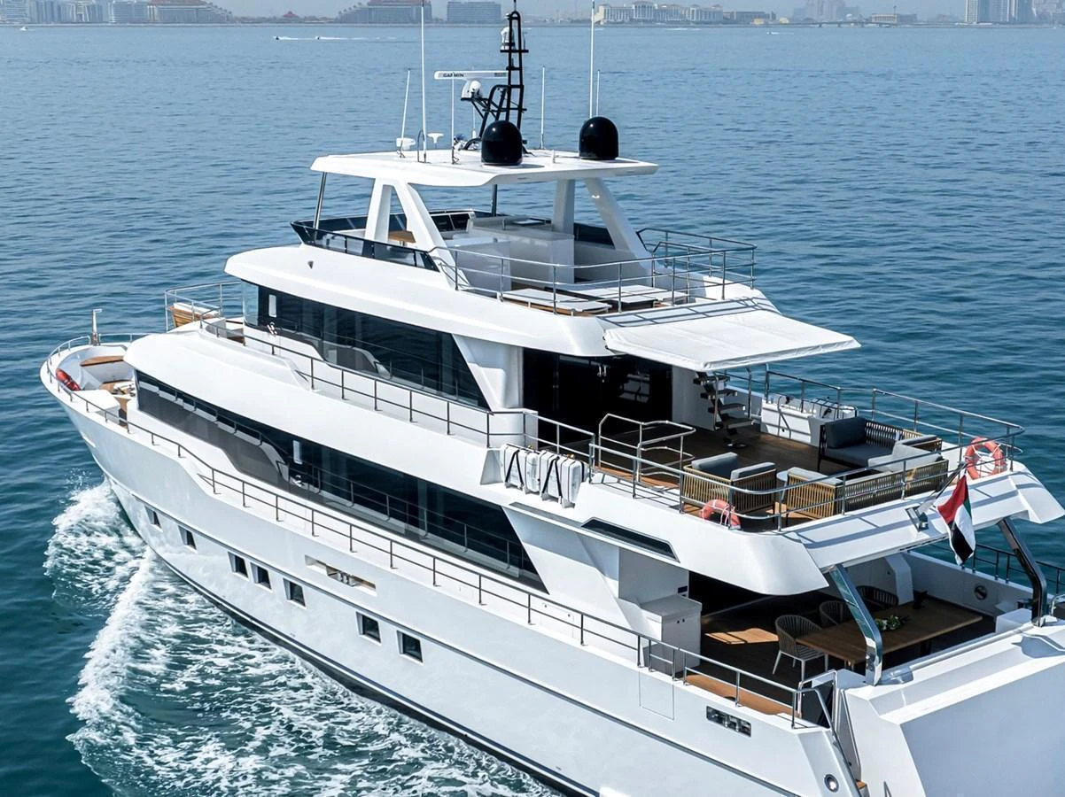 A sleek and modern yacht cruising on calm waters with a cityscape in the background. aboard NOMAD 101 ON-ORDER Yacht for Sale