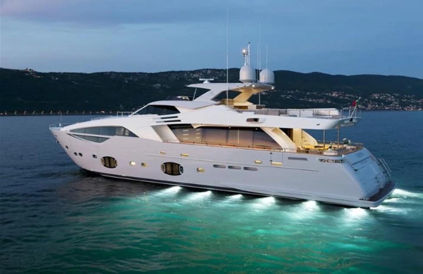 A sleek and modern yacht is illuminated on the water at dusk, showcasing its elegant design and spacious decks. aboard SHA SHA SHA IV Yacht for Sale