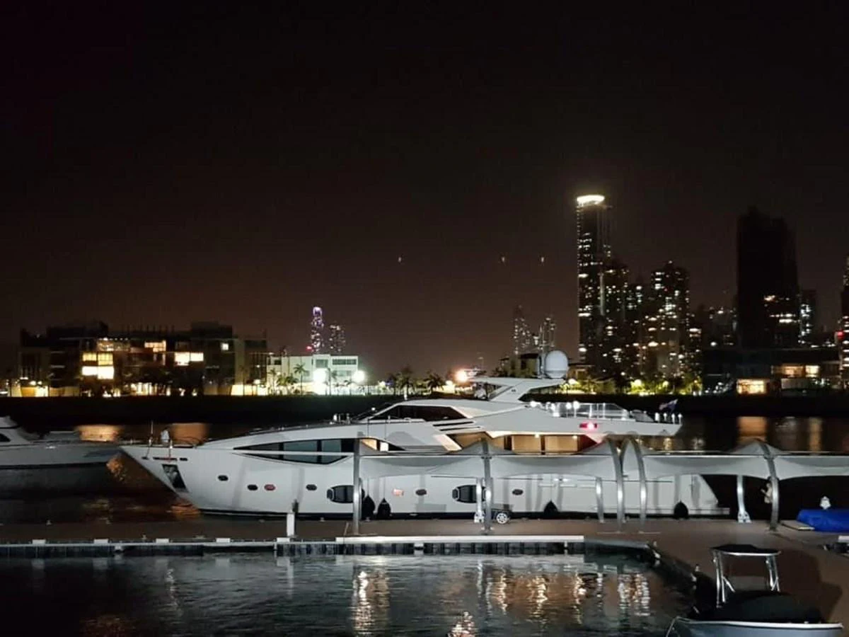 A sleek yacht is docked at night with a city skyline in the background. aboard SHA SHA SHA IV Yacht for Sale