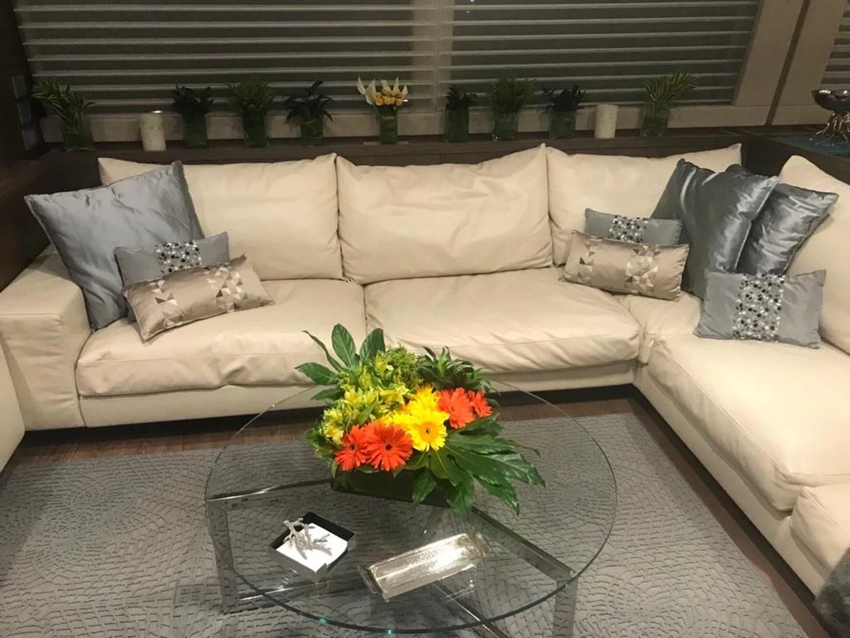 The salon features a comfortable beige sectional sofa adorned with decorative pillows and a glass coffee table with a floral centerpiece. aboard SHA SHA SHA IV Yacht for Sale