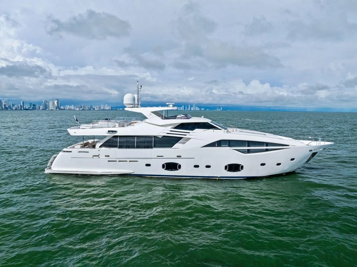 A sleek, modern yacht cruising on calm waters with a cityscape in the background. aboard SHA SHA SHA IV Yacht for Sale