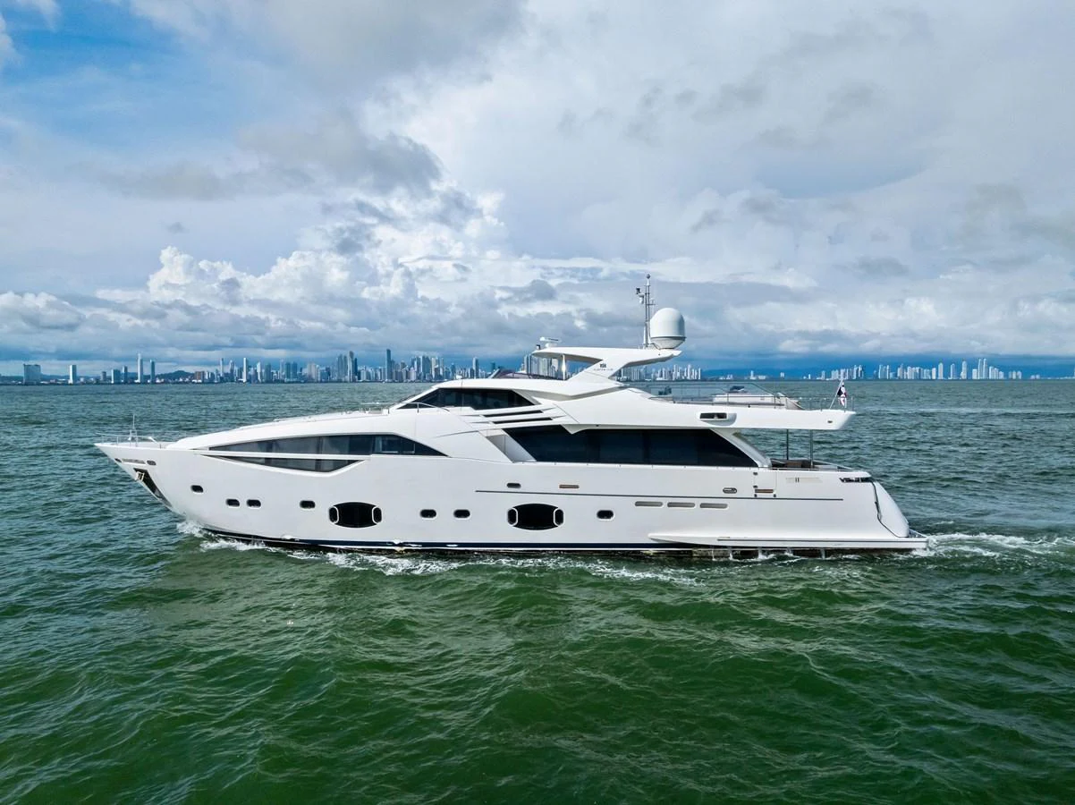 A sleek, modern yacht cruises gracefully on the open water with a city skyline in the background. aboard SHA SHA SHA IV Yacht for Sale
