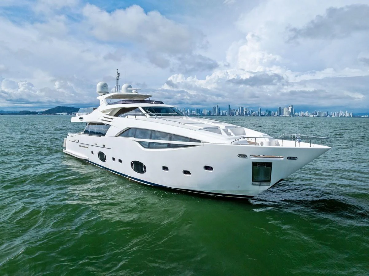 A sleek and modern yacht glides through the water with a cityscape in the background. aboard SHA SHA SHA IV Yacht for Sale