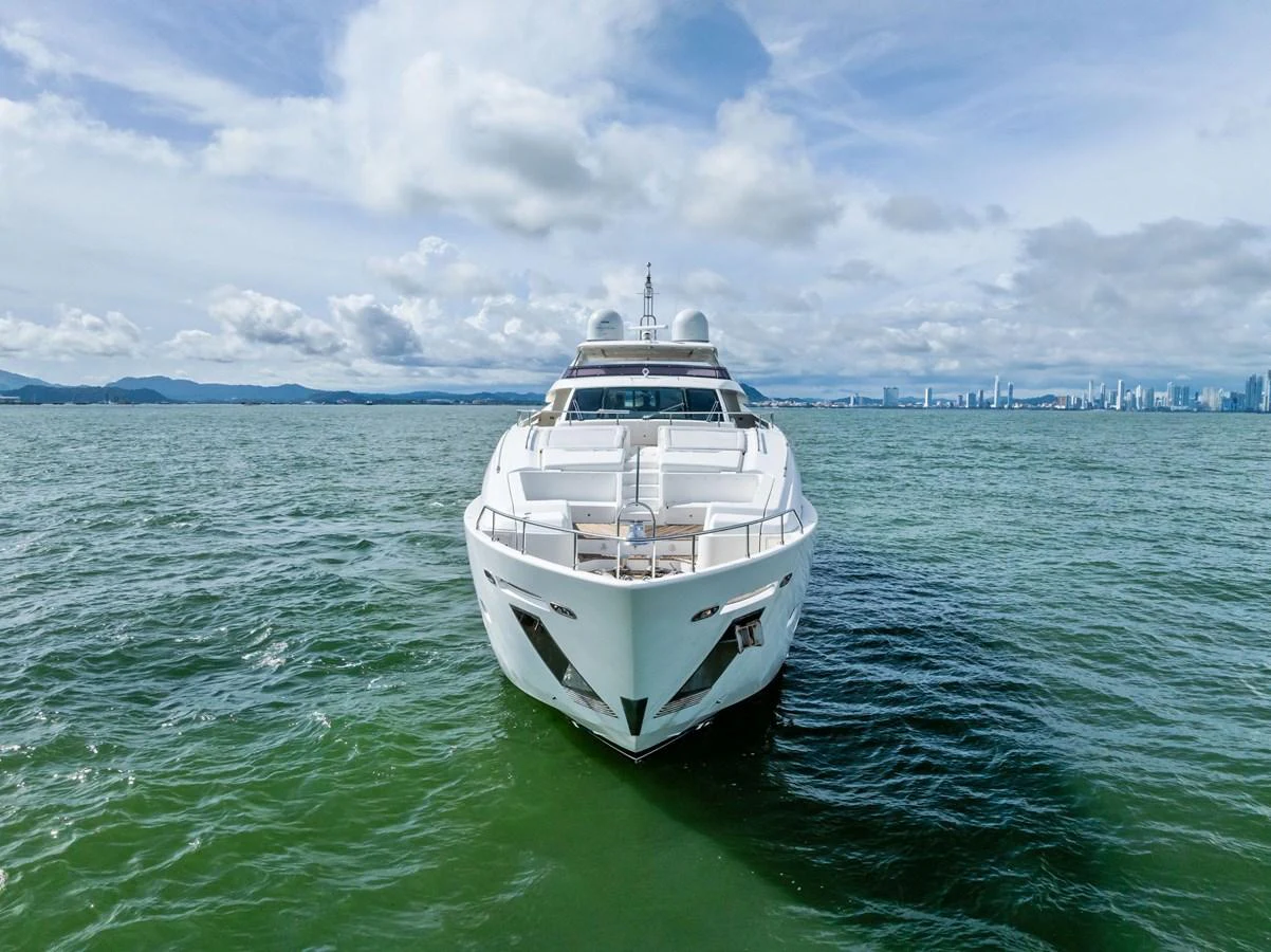 A sleek yacht is cruising on calm waters with a cityscape in the background. aboard SHA SHA SHA IV Yacht for Sale