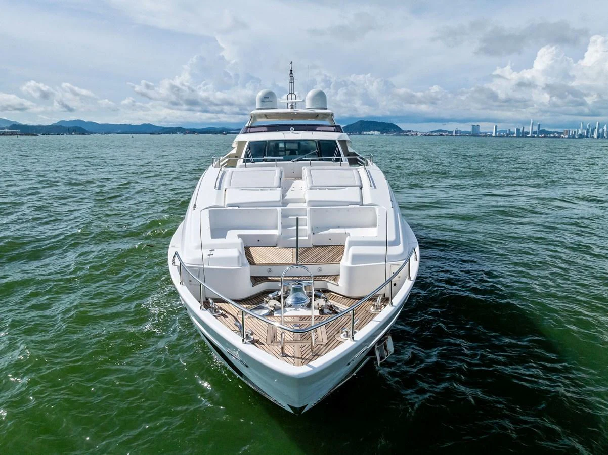 A sleek yacht cruising on calm waters with a cityscape in the background. aboard SHA SHA SHA IV Yacht for Sale