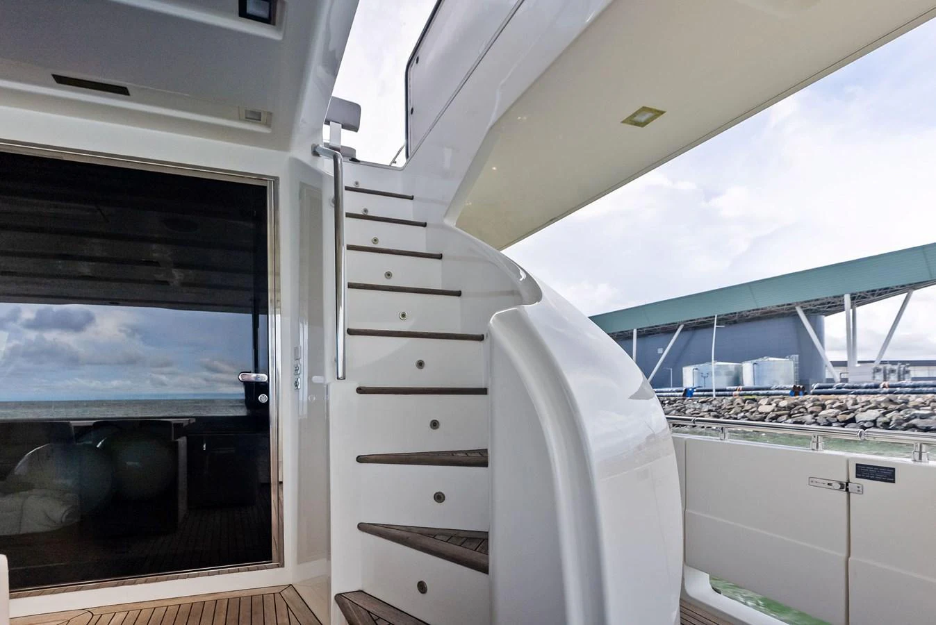 The aft deck features a sleek staircase leading to the upper levels, with a view of the marina in the background. aboard SHA SHA SHA IV Yacht for Sale