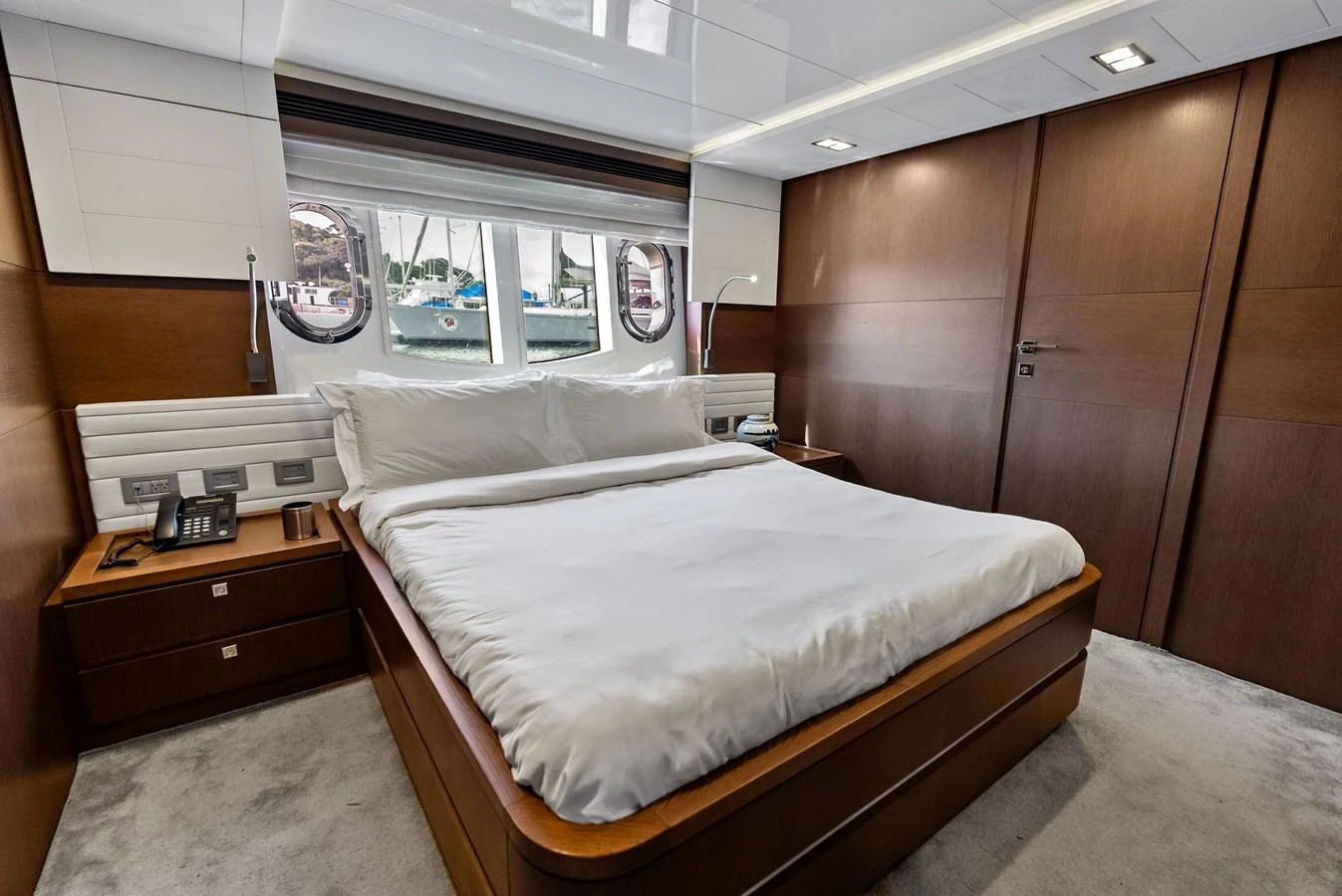 The stateroom features a luxurious bed with a view of the sea through round windows. aboard SHA SHA SHA IV Yacht for Sale