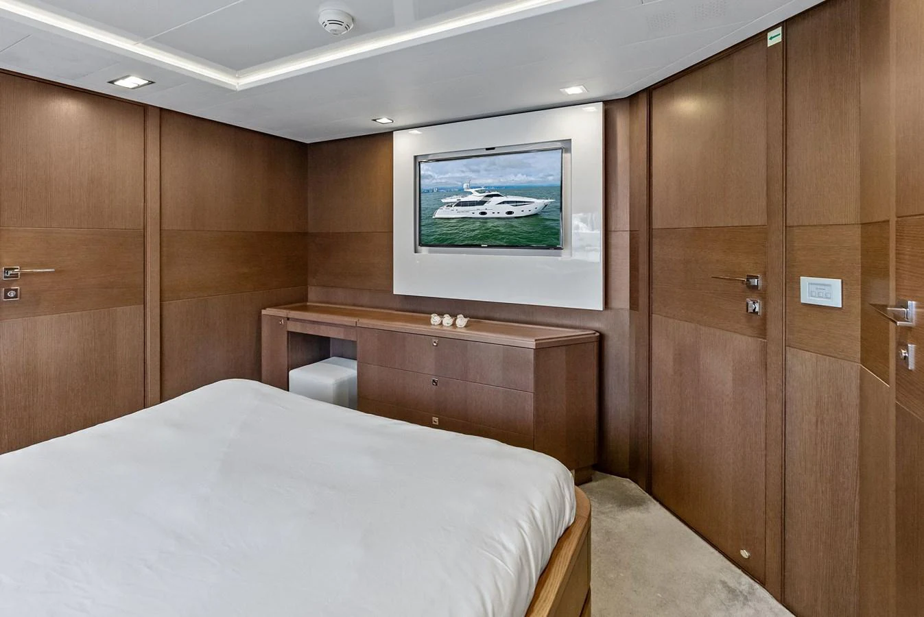 The stateroom features elegant wood paneling, a comfortable bed, and a large wall-mounted TV displaying a yacht image. aboard SHA SHA SHA IV Yacht for Sale