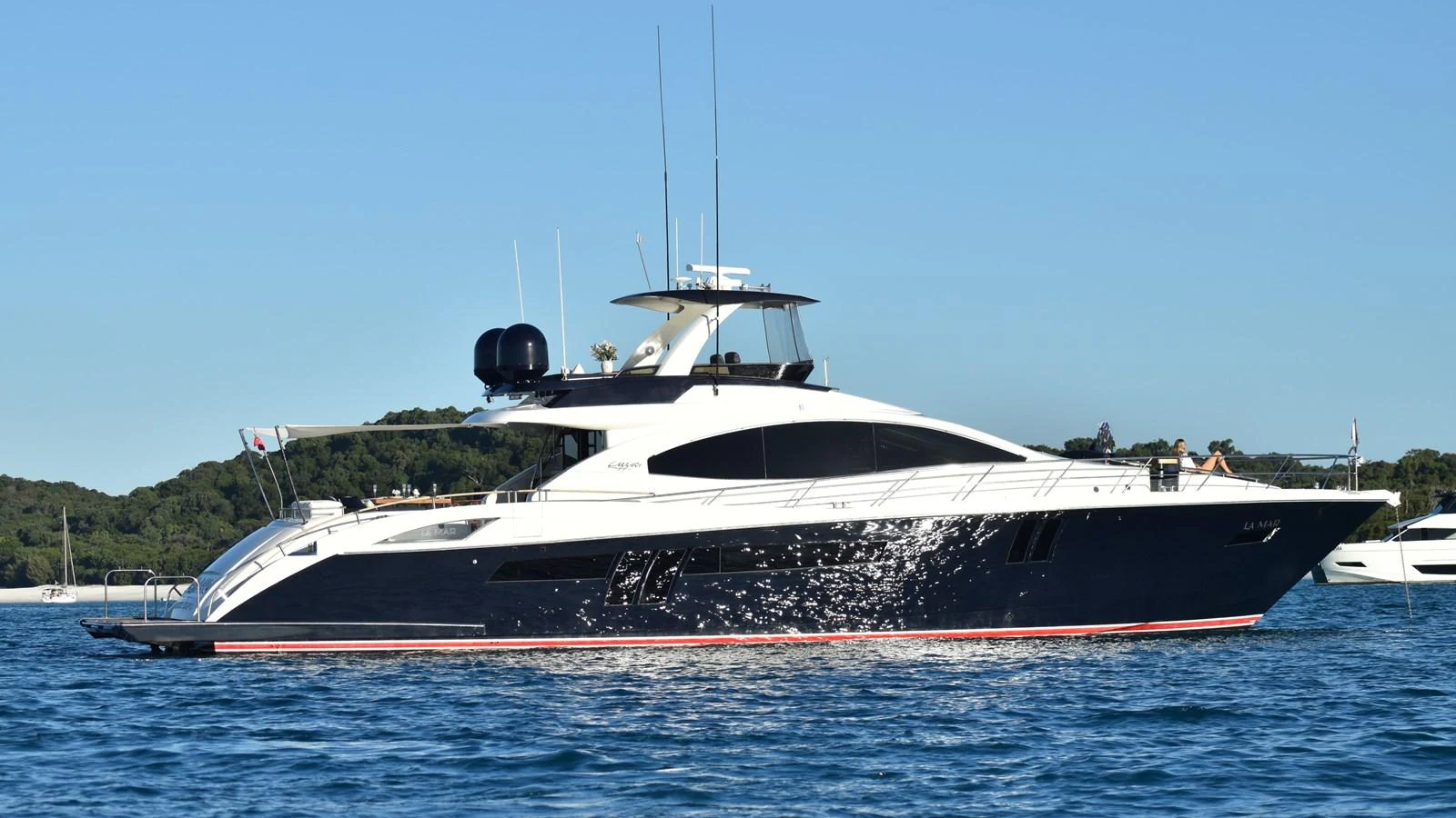 A sleek and modern yacht glides gracefully on the water against a backdrop of lush greenery. aboard LA MAR Yacht for Sale