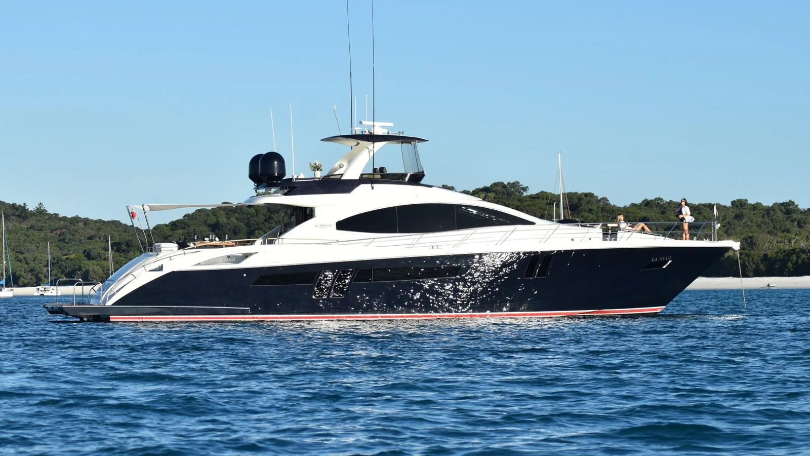 A sleek and modern yacht glides gracefully on calm waters against a backdrop of lush greenery. aboard LA MAR Yacht for Sale