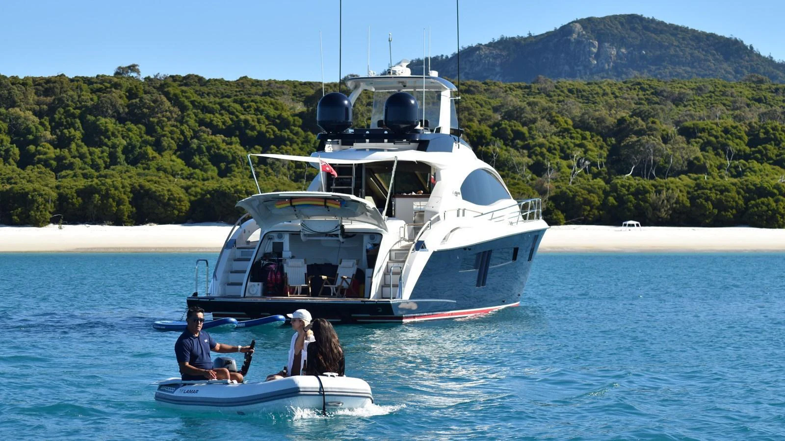 A luxurious yacht anchored near a pristine beach with people enjoying a tender ride. aboard LA MAR Yacht for Sale