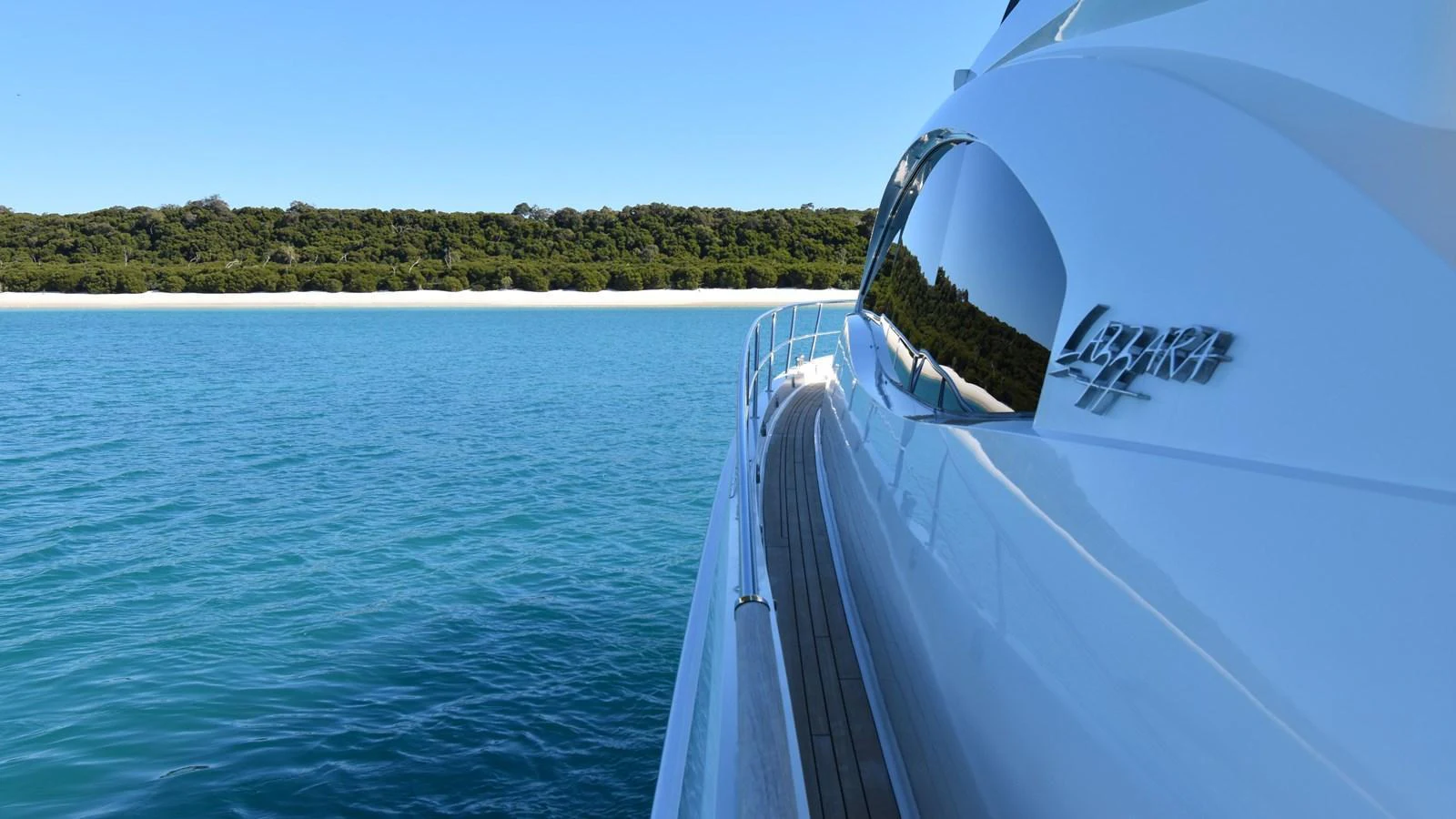 A sleek yacht cruising along a serene coastline with clear blue waters and a lush green backdrop. aboard LA MAR Yacht for Sale