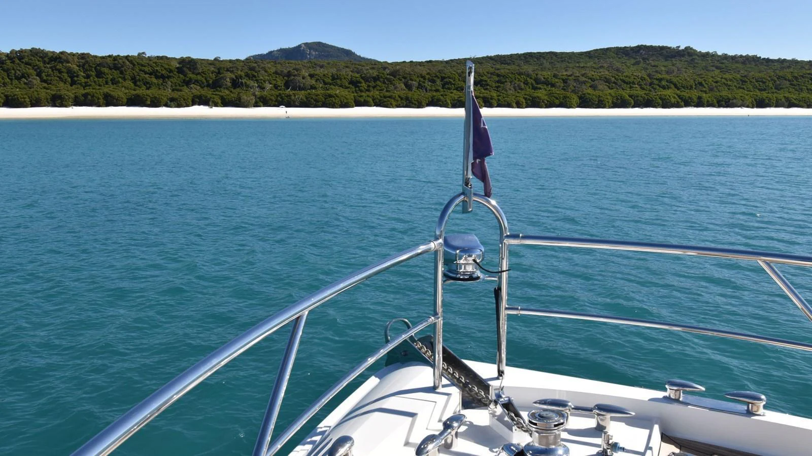 The yacht's bow overlooks a serene, turquoise sea with a lush, green coastline in the distance. aboard LA MAR Yacht for Sale