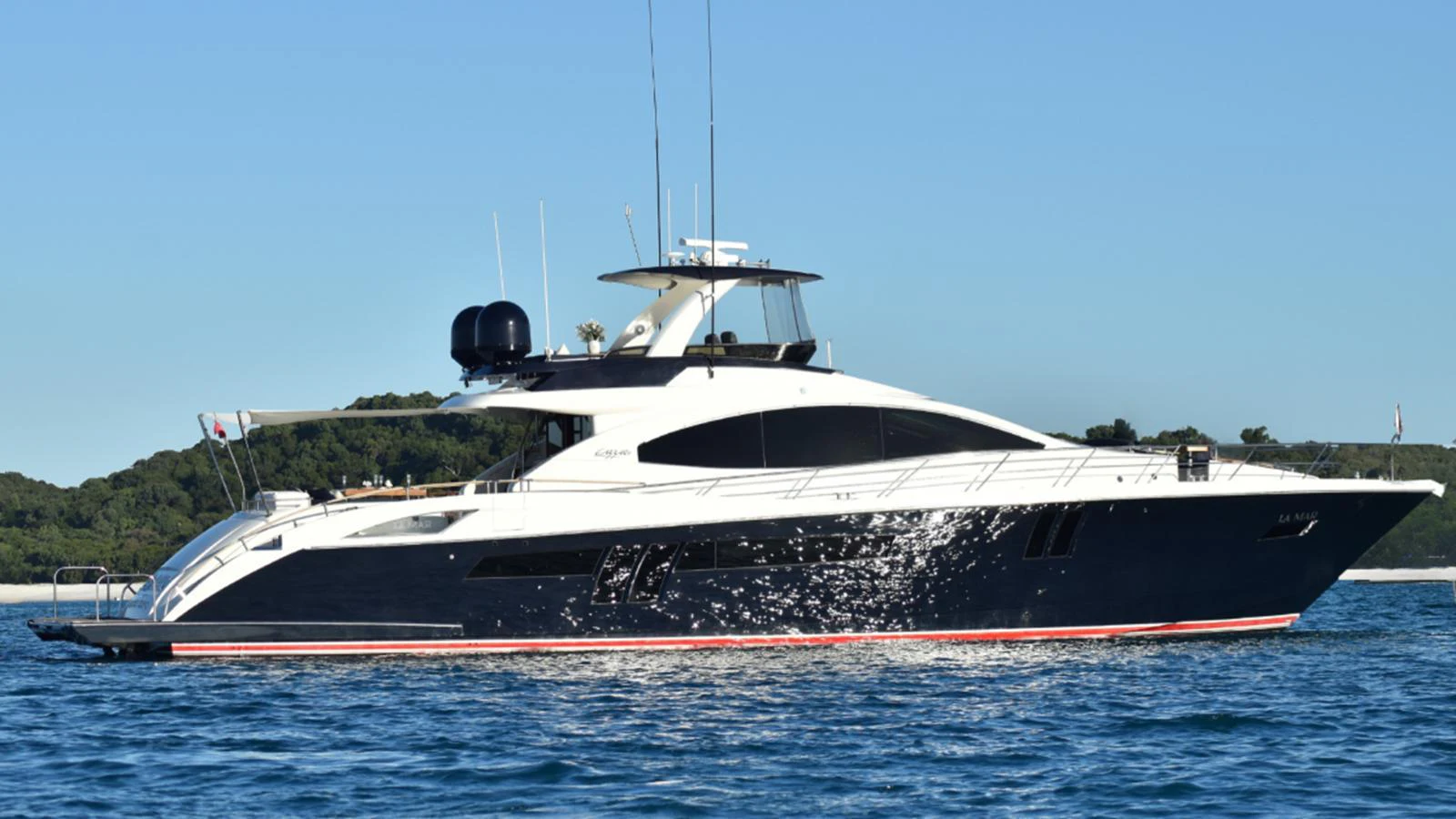 A sleek and modern yacht glides gracefully on the water against a backdrop of lush greenery. aboard LA MAR Yacht for Sale