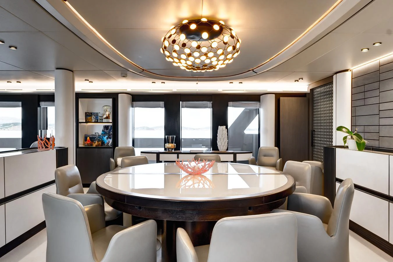 The yacht's dining area features a large circular table surrounded by plush chairs, under a modern, artistic light fixture. aboard L.A.U.L. Yacht for Sale