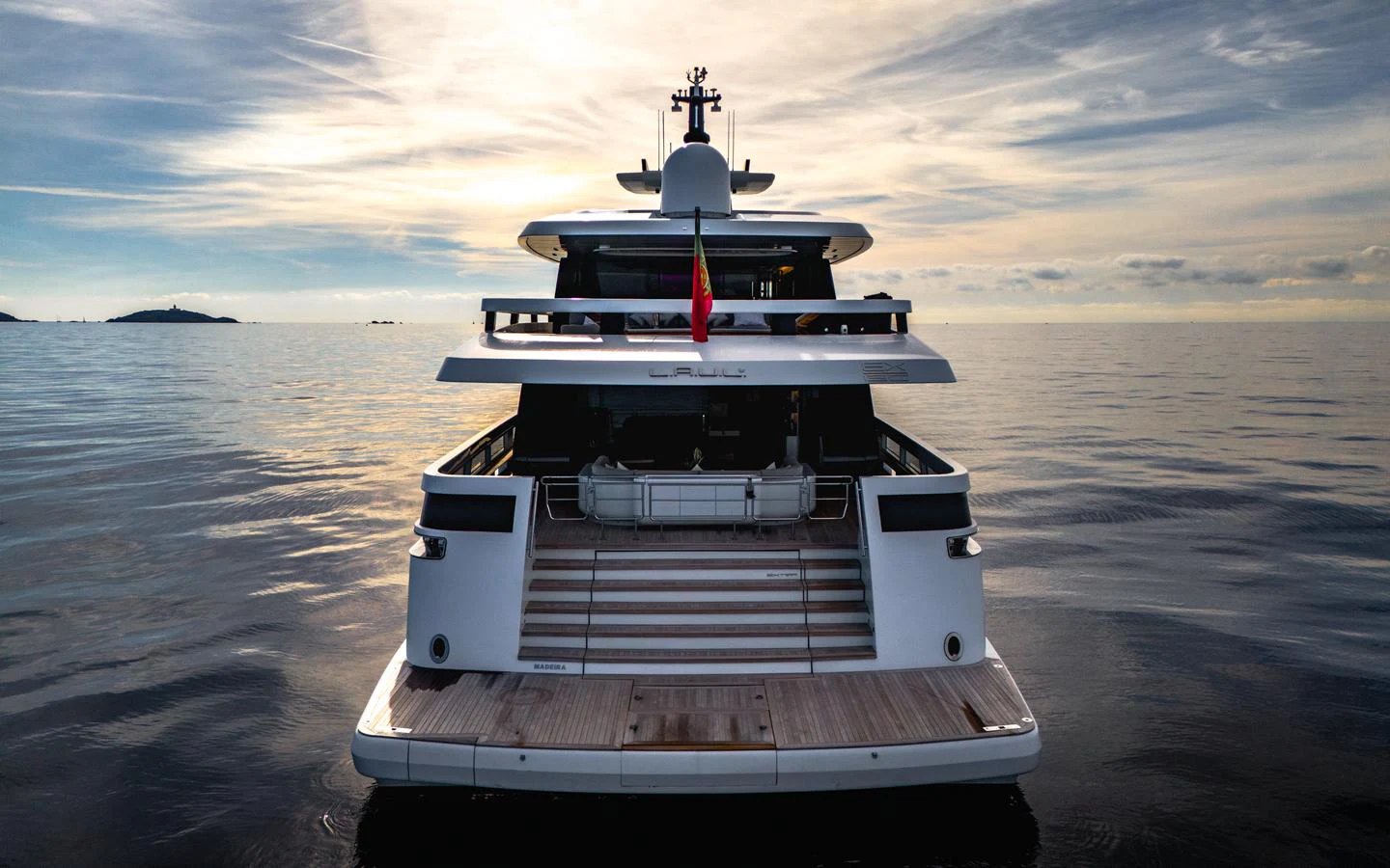 A luxurious yacht is seen from the rear, floating serenely on calm waters under a dramatic sky. aboard L.A.U.L. Yacht for Sale