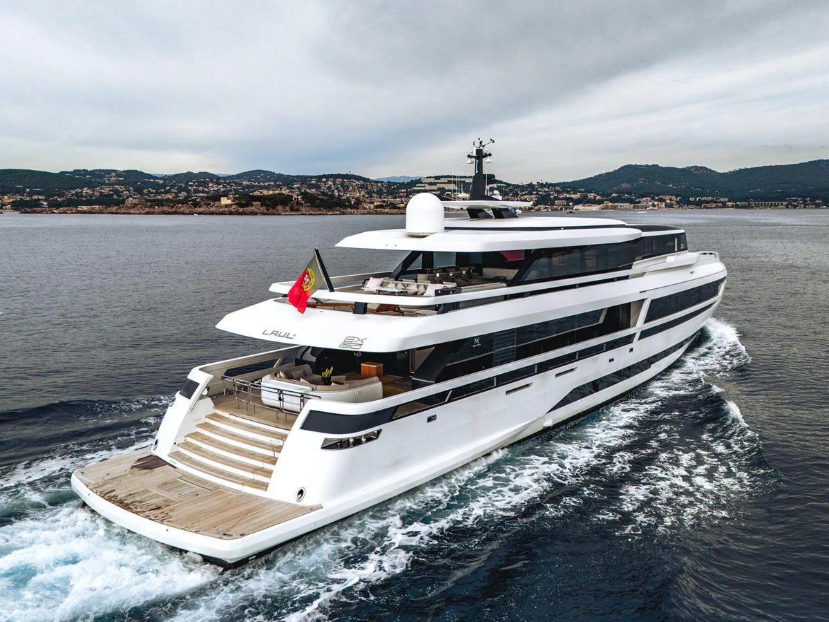 A sleek, modern yacht cruises through calm waters with a scenic coastal backdrop. aboard L.A.U.L. Yacht for Sale