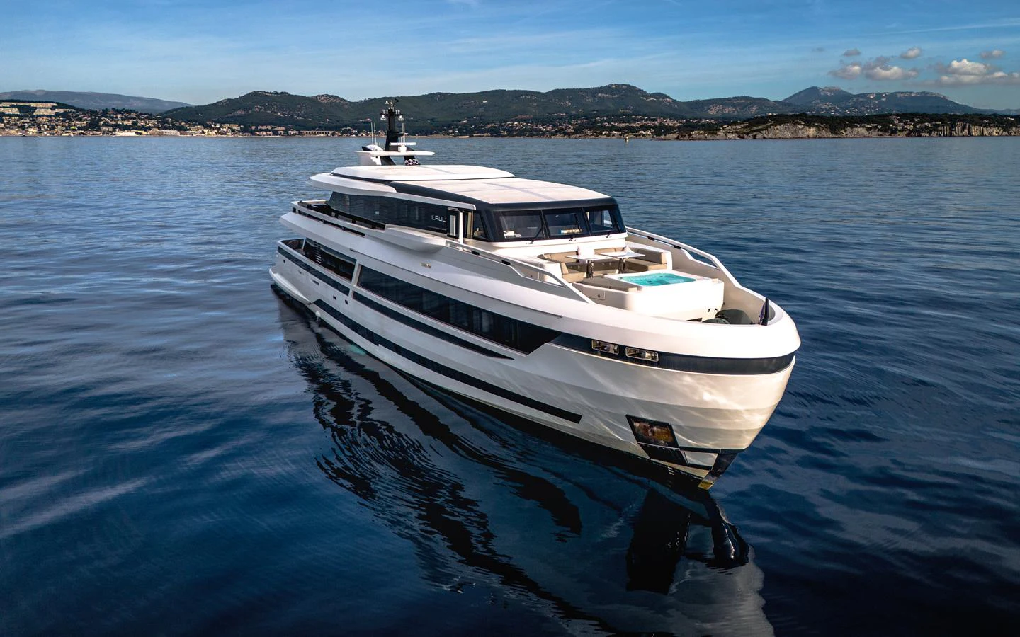 A sleek and modern yacht glides gracefully on calm waters with a stunning backdrop of mountains and coastline. aboard L.A.U.L. Yacht for Sale