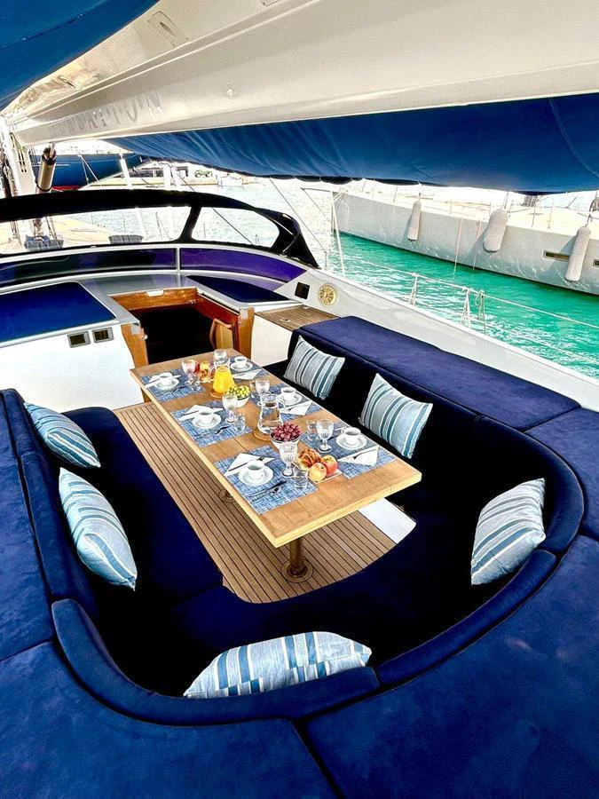 An elegant dining area on the yacht, featuring a beautifully set table surrounded by plush blue seating with a view of the water. aboard PERSISTENCE Yacht for Sale