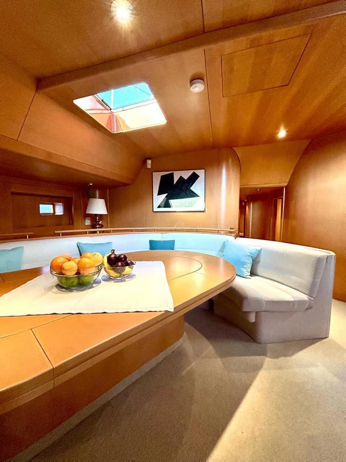 The yacht's dining area features a cozy, curved seating arrangement with a wooden table and modern decor. aboard PERSISTENCE Yacht for Sale