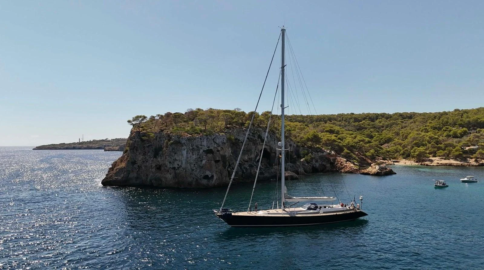 A sleek yacht sails gracefully on calm waters near a rocky coastline. aboard PERSISTENCE Yacht for Sale