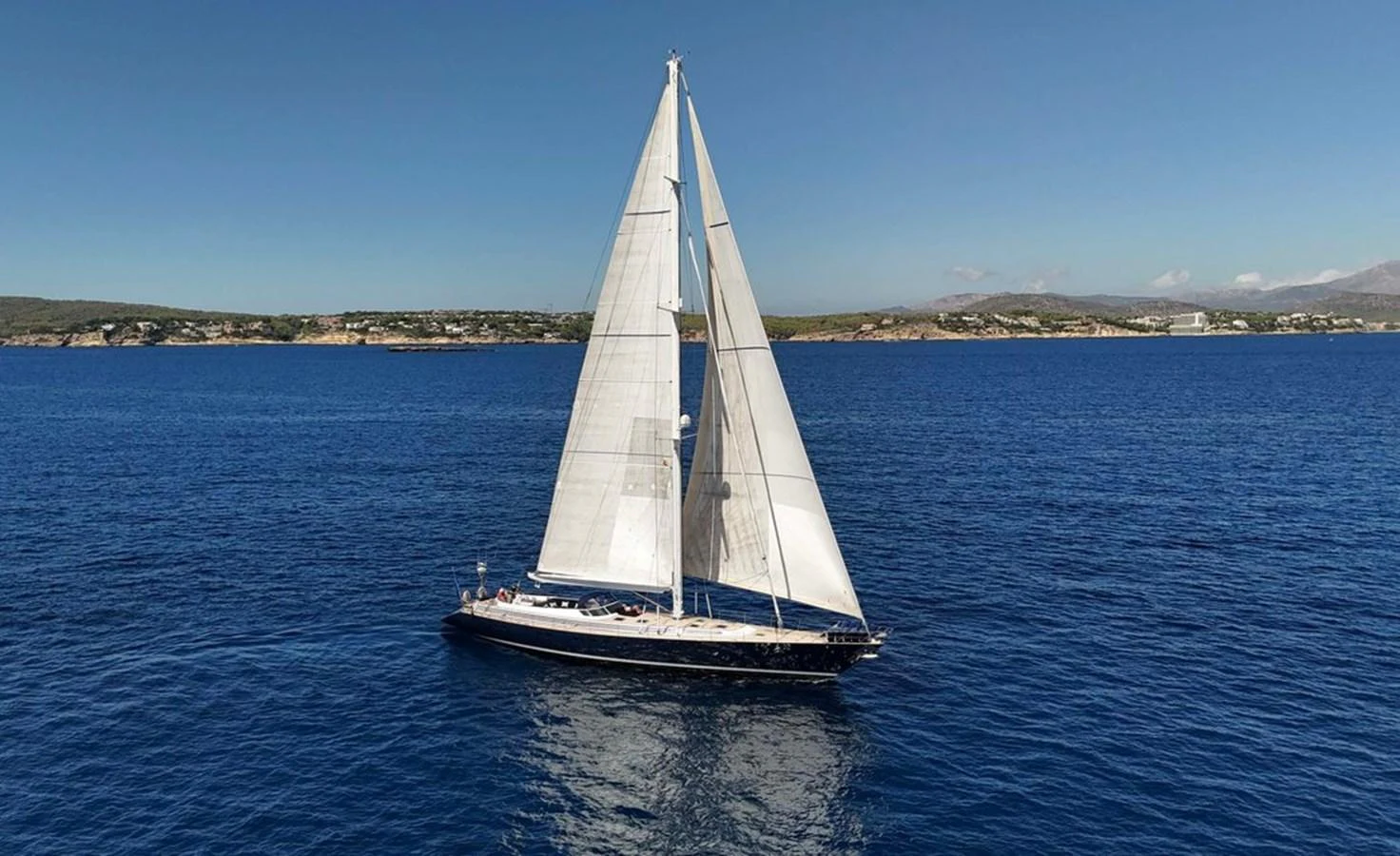 A sleek sailing yacht glides gracefully on the open sea under clear blue skies. aboard PERSISTENCE Yacht for Sale