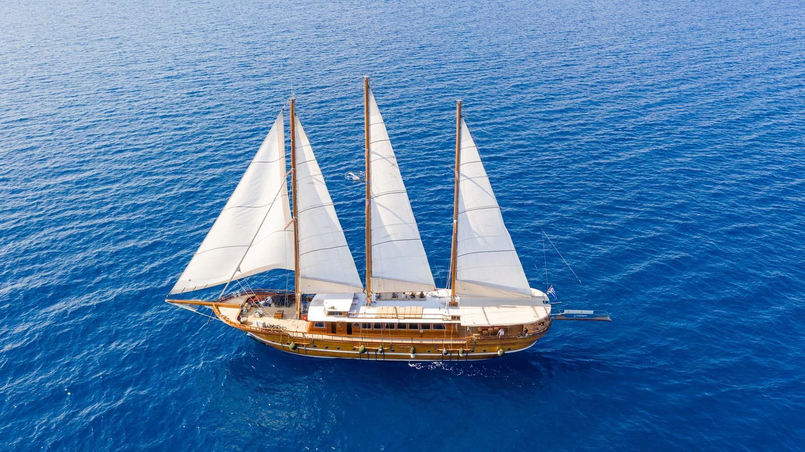 A classic sailing yacht with three masts glides gracefully over the deep blue sea. aboard THALASSA Yacht for Sale