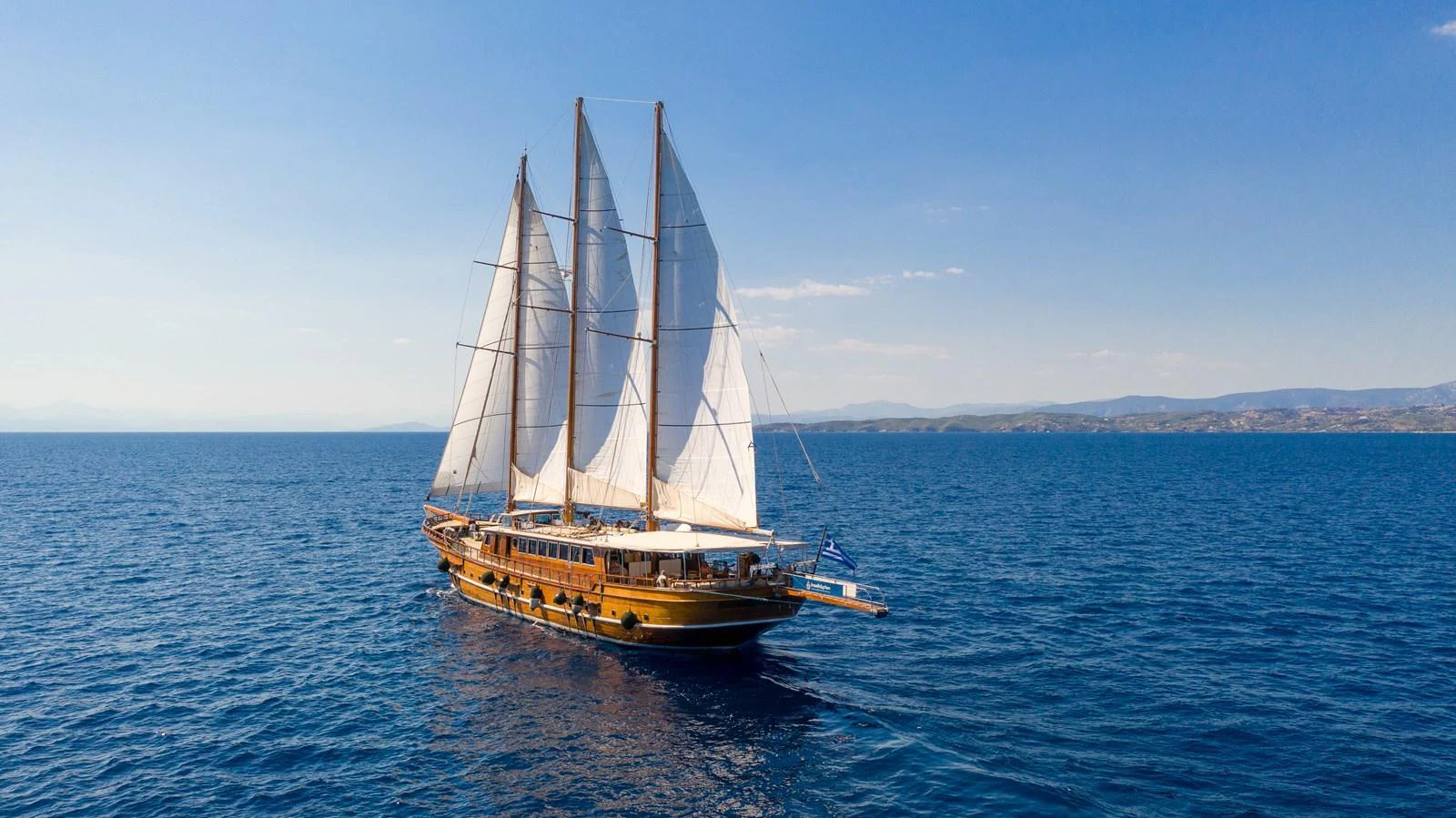 A classic sailing yacht glides gracefully over the deep blue sea under clear skies. aboard THALASSA Yacht for Sale