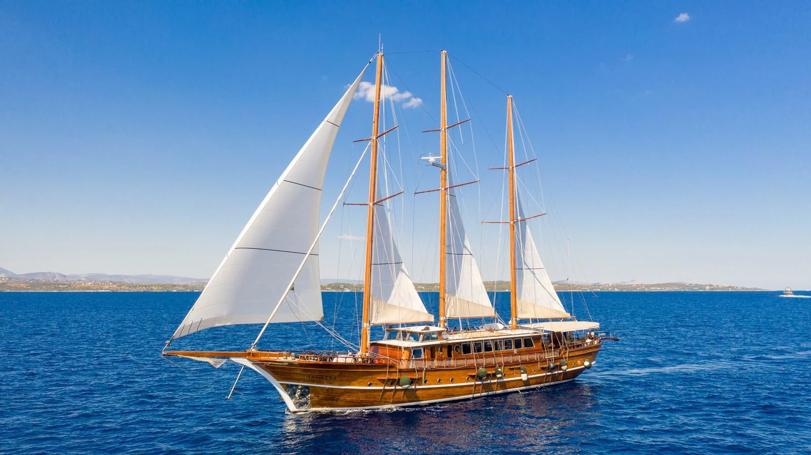 A stunning classic sailing yacht glides gracefully on the open sea under clear blue skies. aboard THALASSA Yacht for Sale
