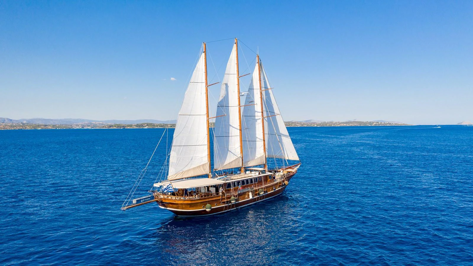 A classic sailing yacht glides gracefully over the deep blue sea under a clear sky. aboard THALASSA Yacht for Sale