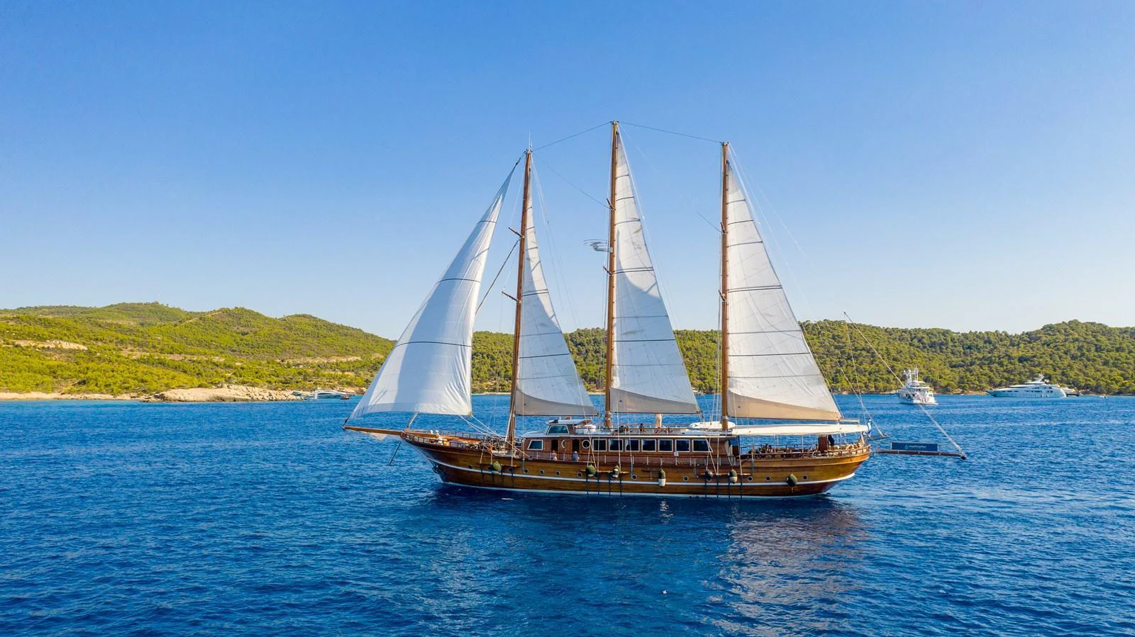 A classic sailing yacht glides gracefully on the serene blue waters with its sails fully unfurled. aboard THALASSA Yacht for Sale