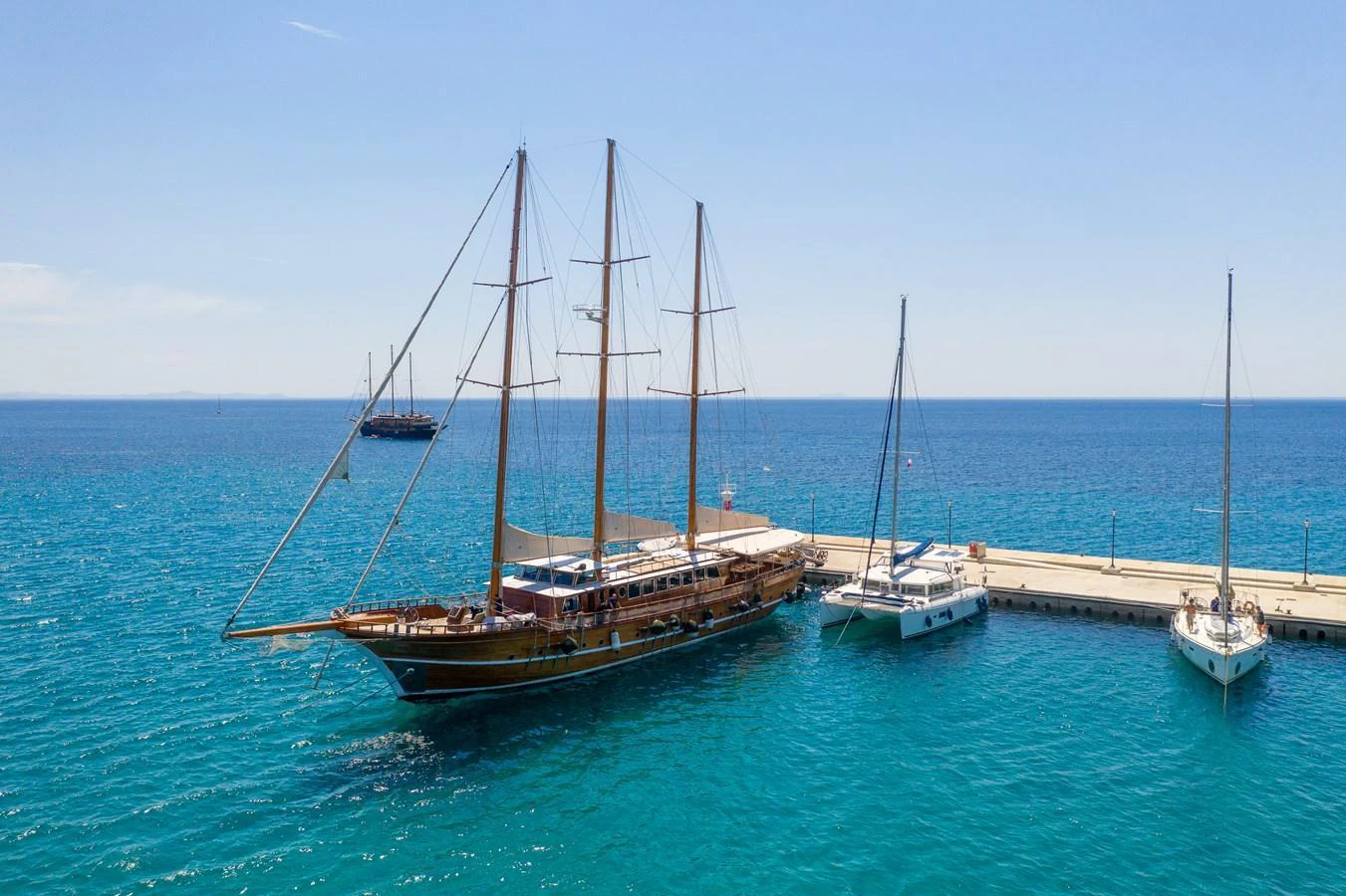 A classic sailing yacht is docked at a serene marina, showcasing its elegant wooden structure and tall masts. aboard THALASSA Yacht for Sale