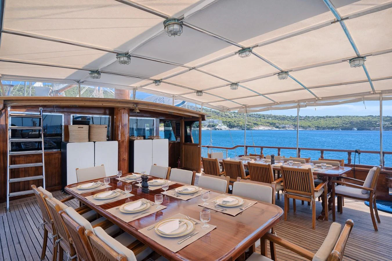 The yacht features a spacious alfresco dining area with elegant wooden furniture and a stunning view of the sea. aboard THALASSA Yacht for Sale