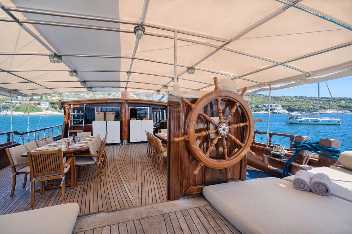 The aft deck features a spacious dining area and a classic wooden helm under a shaded canopy. aboard THALASSA Yacht for Sale