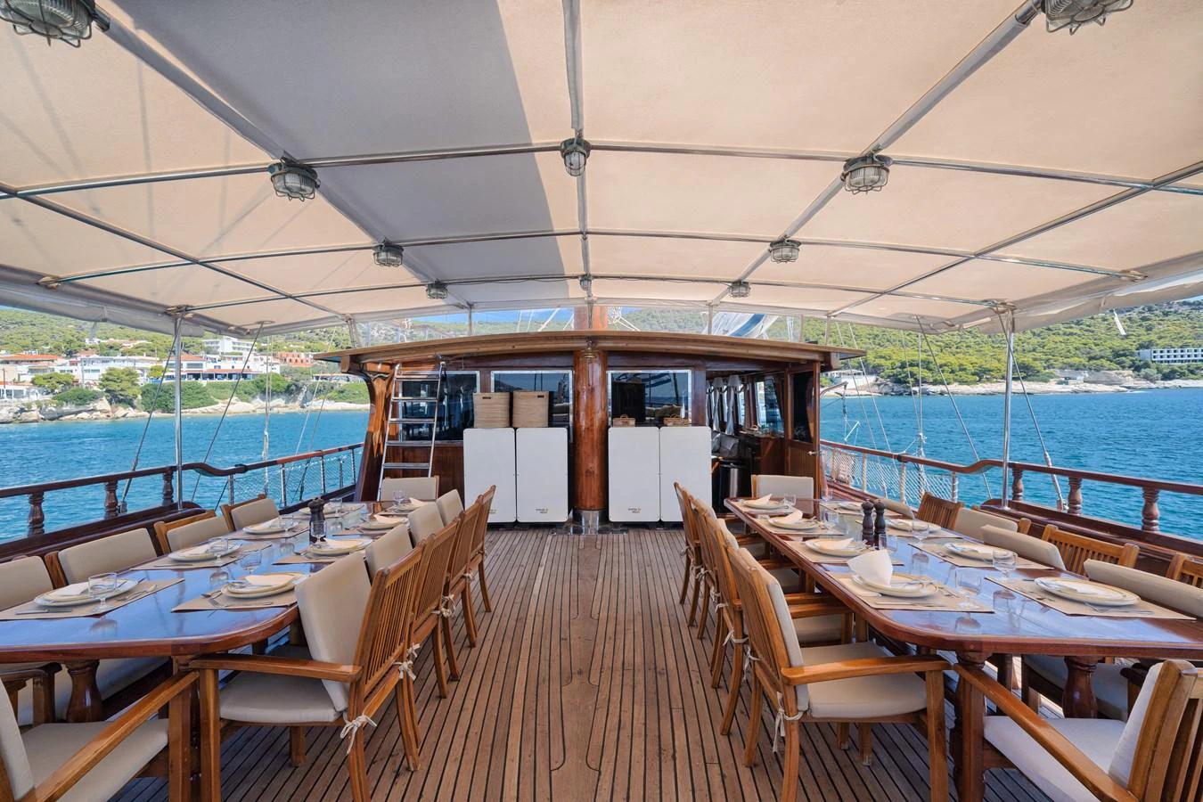 The aft deck features an elegant dining area with two long tables set for a meal, under a shaded canopy. aboard THALASSA Yacht for Sale