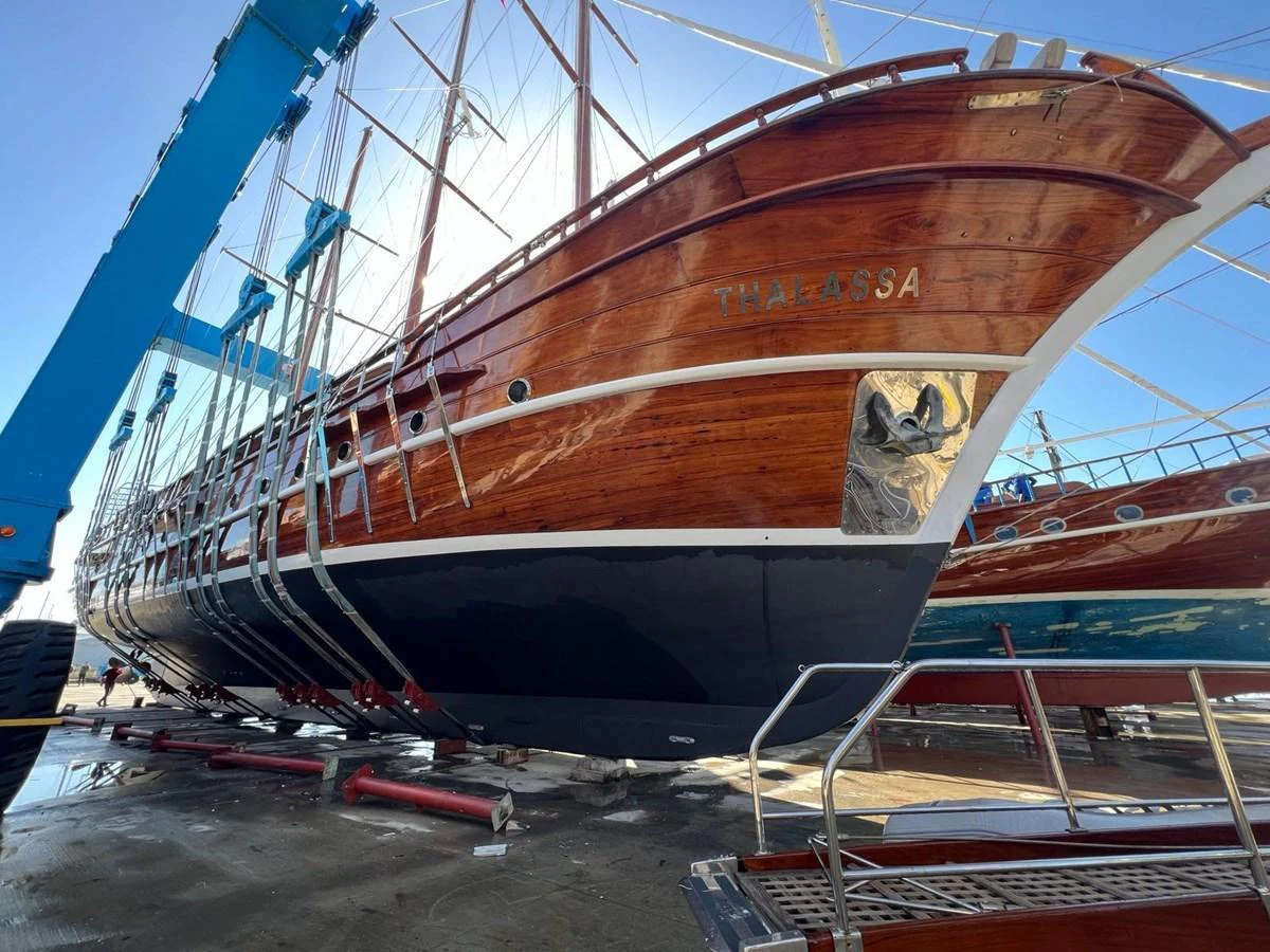 A classic wooden yacht is being lifted out of the water for maintenance. aboard THALASSA Yacht for Sale