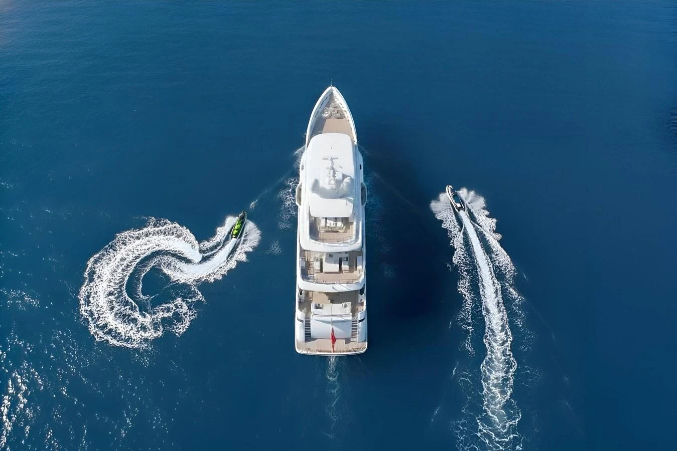 Aerial view of a yacht cruising with two smaller watercrafts creating dynamic patterns in the water. aboard OSKAR ONE Yacht for Sale