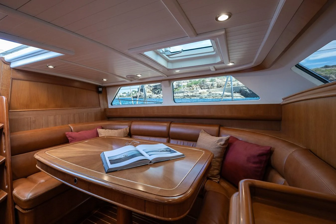 The saloon features a cozy seating area with a wooden table and ample natural light from the windows and skylights. aboard TEMPEST Yacht for Sale