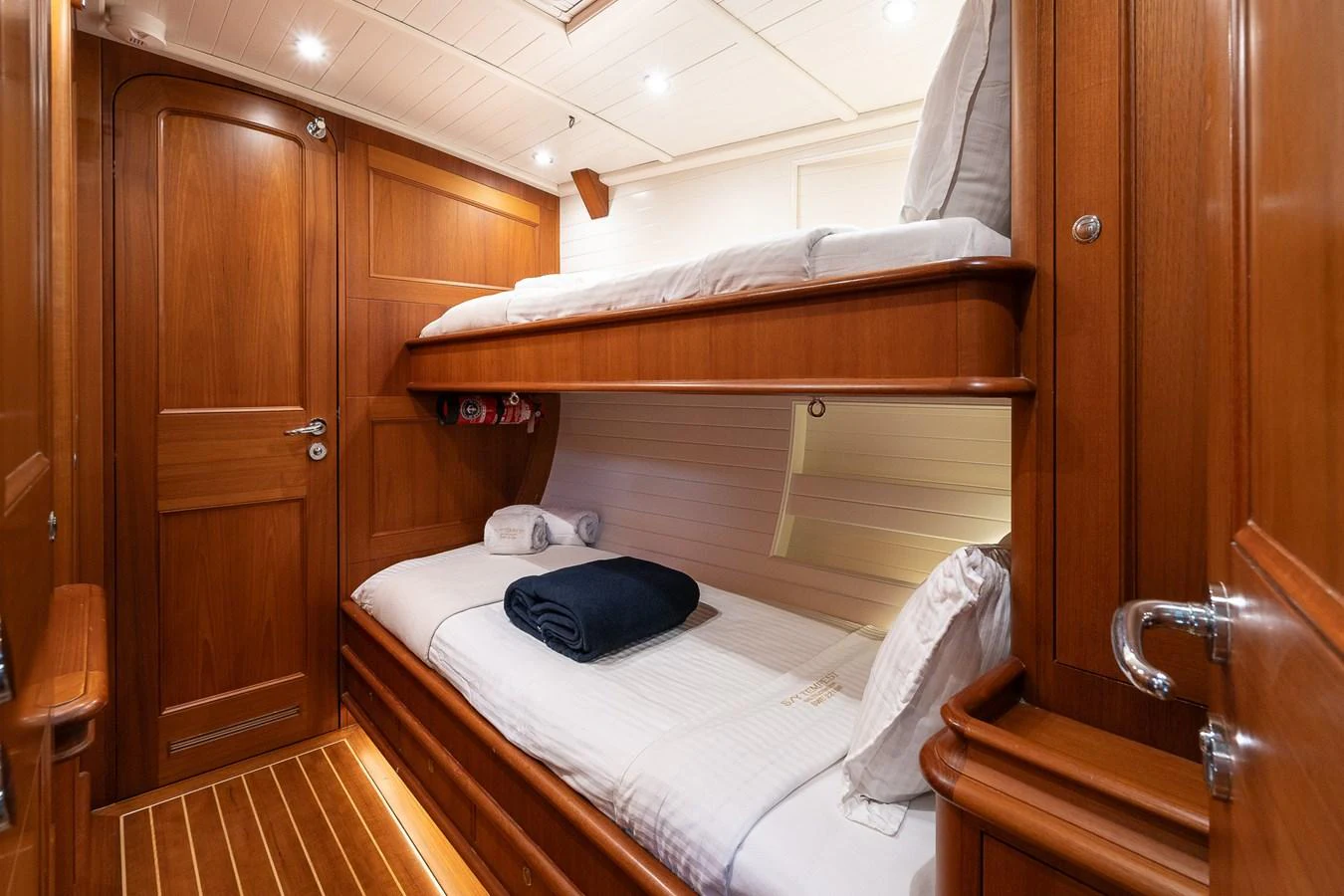 The guest cabin features cozy wooden bunk beds with elegant bedding and ample lighting. aboard TEMPEST Yacht for Sale
