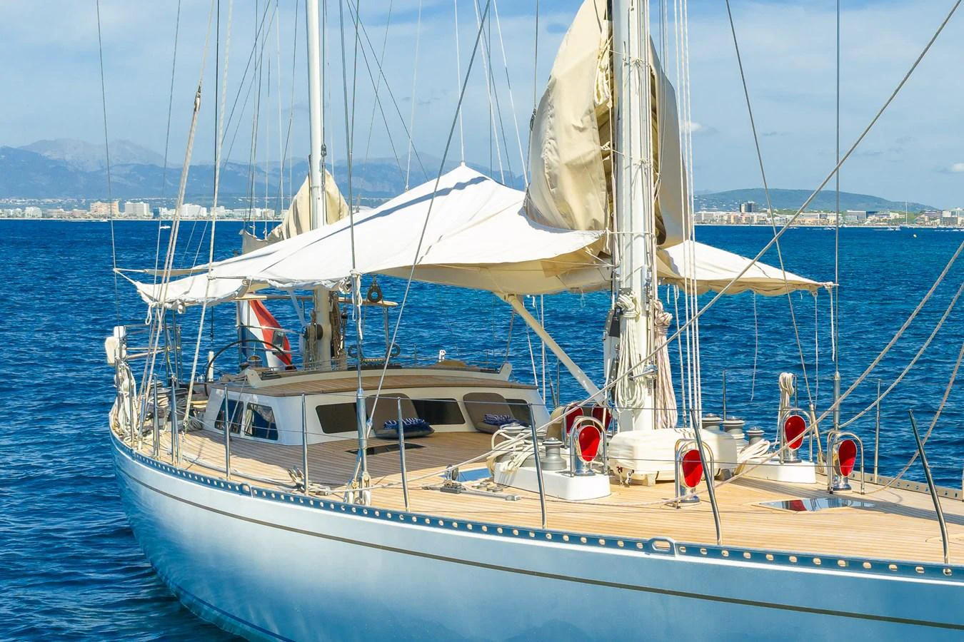 A sleek sailing yacht glides gracefully on calm blue waters with a cityscape in the background. aboard TEMPEST Yacht for Sale