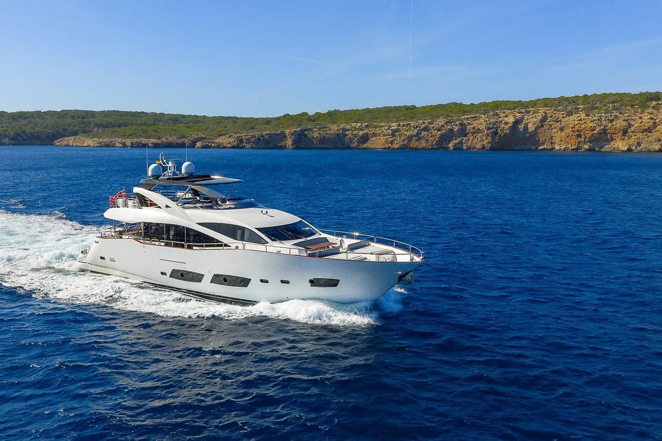 A sleek and modern yacht cruises through clear blue waters with a scenic coastline in the background. aboard THIS TIME NEXT YEAR Yacht for Sale