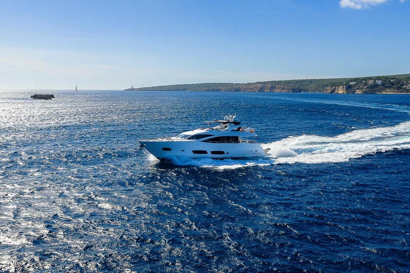 A sleek yacht cruises through vibrant blue waters with a scenic coastline in the background. aboard THIS TIME NEXT YEAR Yacht for Sale