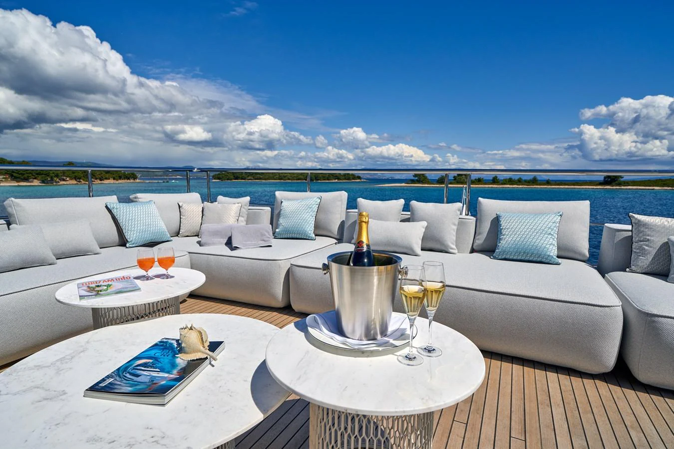 a white couch with a table and a glass of wine on a table with a view of the aboard ALUMINIA TOO Yacht for Sale