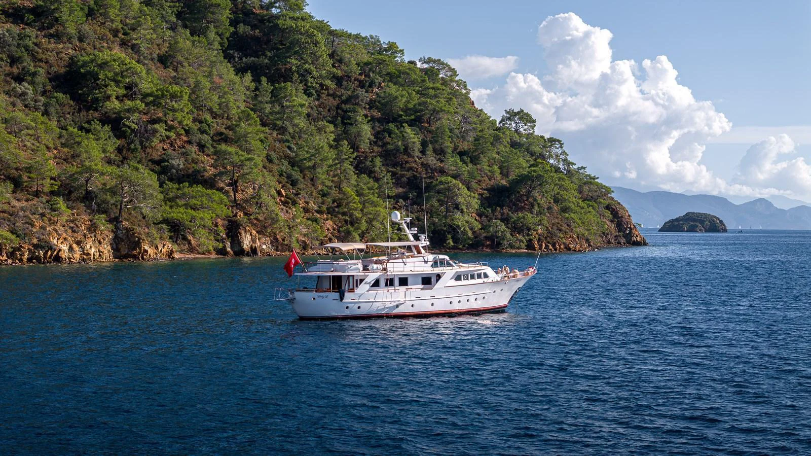 A classic yacht cruises along a scenic coastline with lush greenery and clear blue waters. aboard LADY L Yacht for Sale
