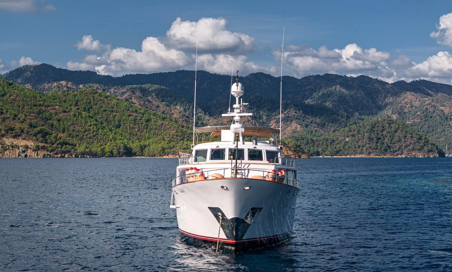 A majestic yacht is anchored in a serene bay with a backdrop of lush hills and a clear blue sky. aboard LADY L Yacht for Sale