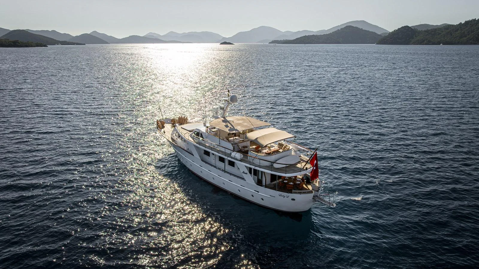 A classic yacht cruises gracefully on calm waters with scenic mountains in the background. aboard LADY L Yacht for Sale
